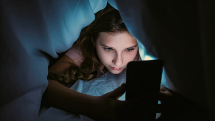 Young woman looking at phone under covers.