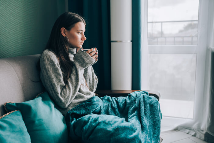 Pensive woman with green blanket looking out window.